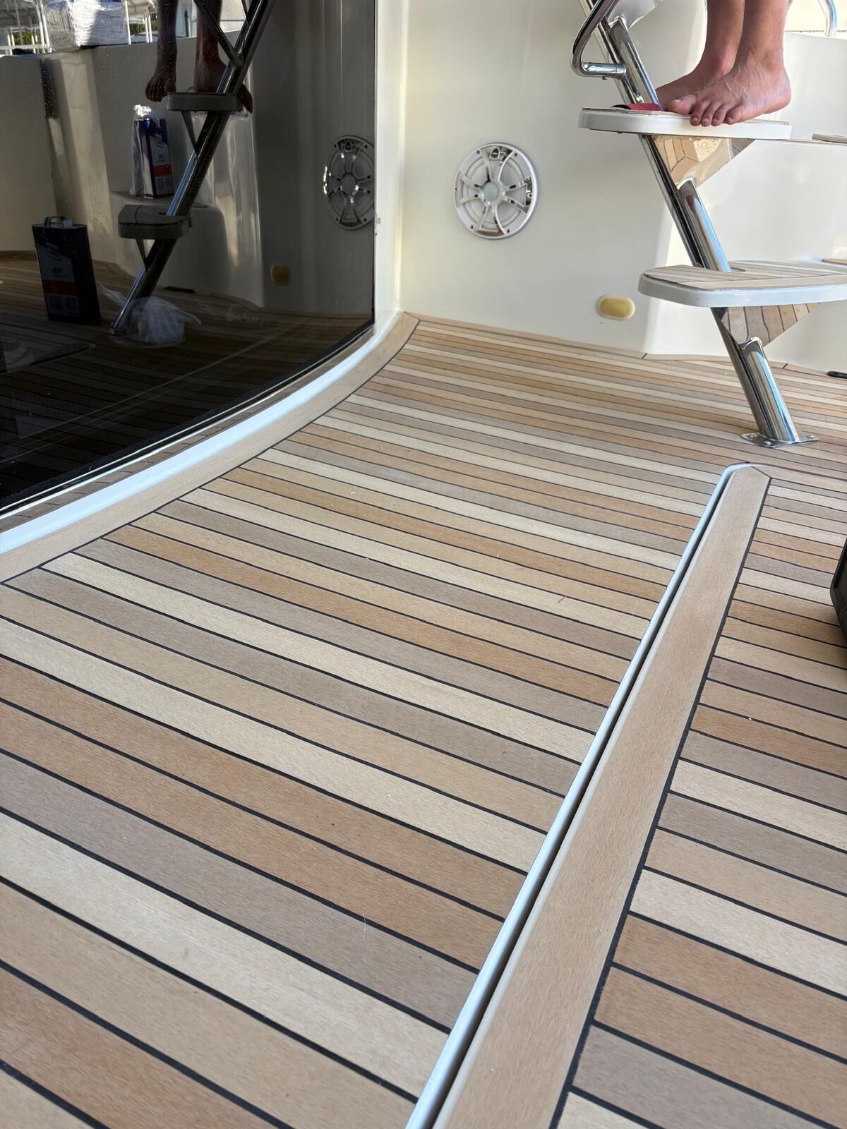 Wide aft deck in synthetic teak with black caulk lines running under a stainless boarding ladder