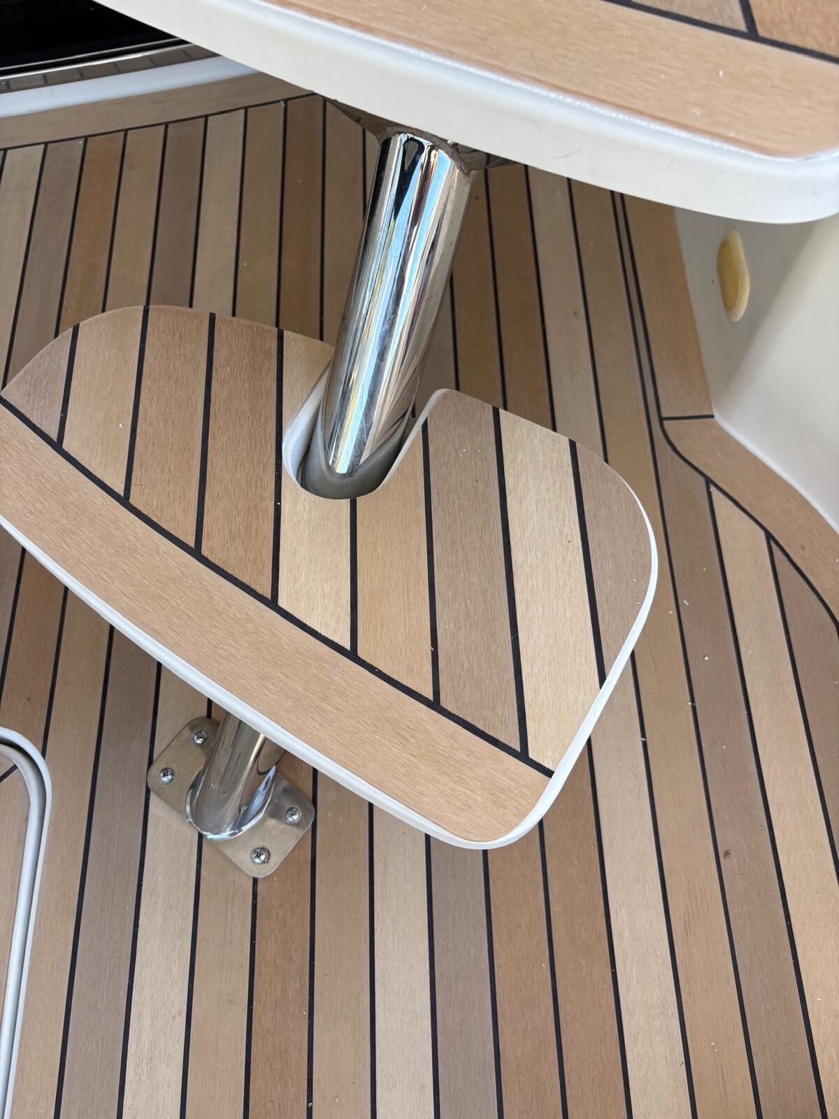 Synthetic teak deck cut in tightly around a stainless seat pedestal with a matching teak-faced footrest