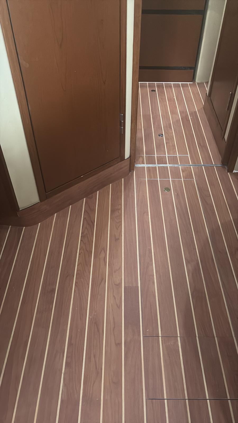 Synthetic teak planking running continuously through a cabin doorway with flush access hatches
