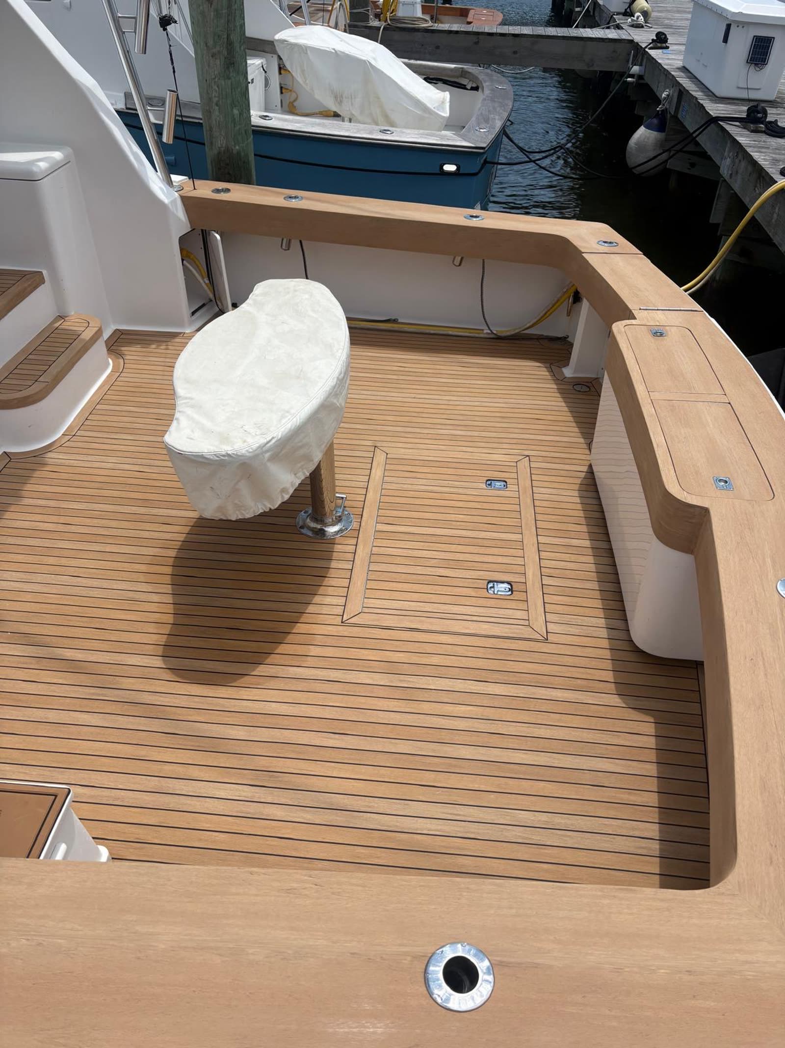 Synthetic teak cockpit sole with a flush deck hatch outlined in caulk lines and stainless lifting rings