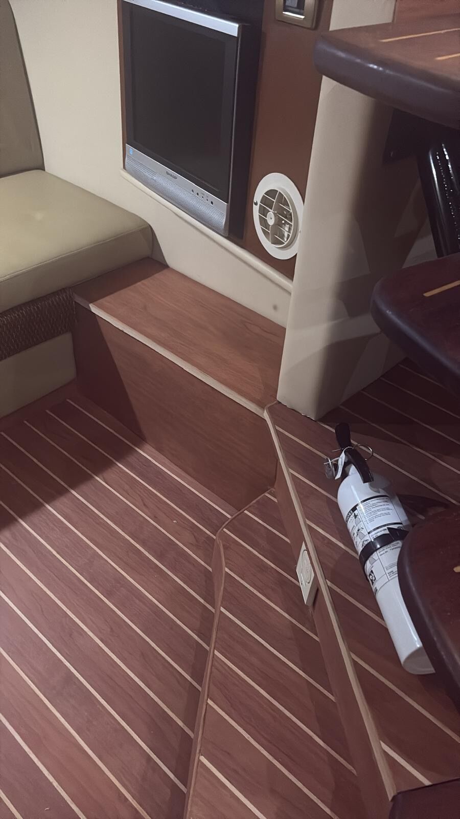 Interior cabin sole laid in dark mahogany synthetic planking with pale caulk lines running past a settee and dinette