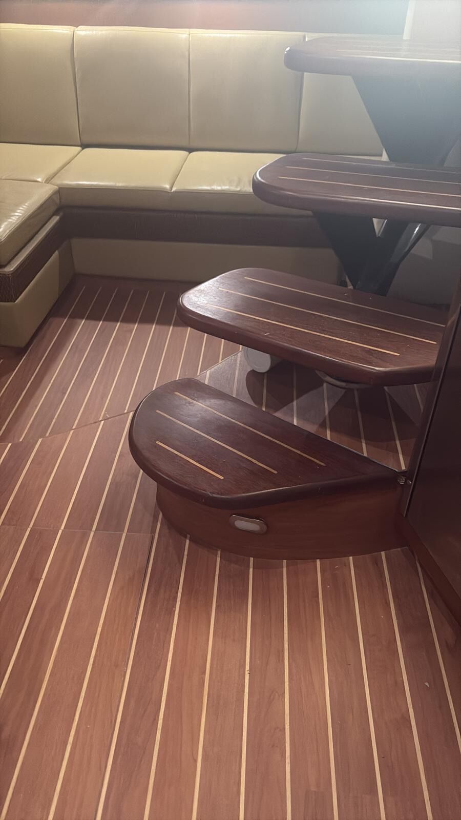 Yacht saloon sole in dark mahogany synthetic planking with pale seams beside varnished companionway steps