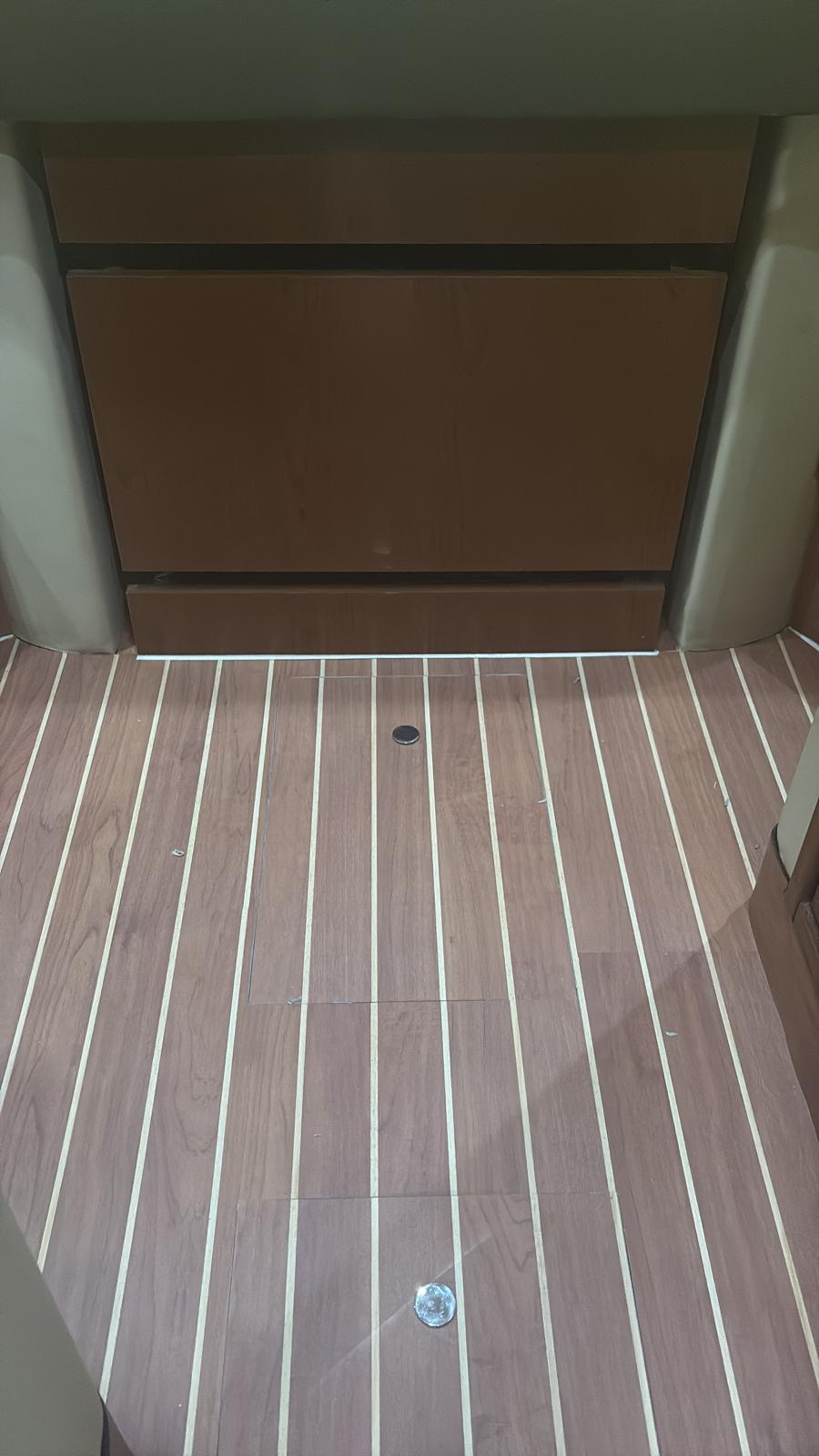 Yacht saloon sole in warm synthetic teak with pale caulk lines running the length of the cabin