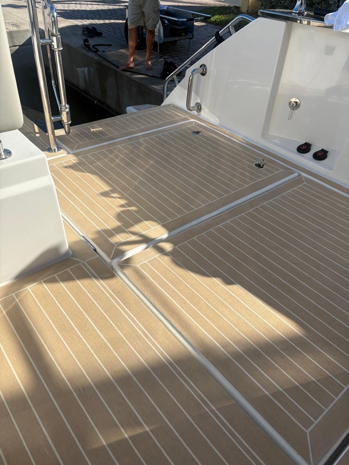Sand synthetic teak cockpit sole with white caulk lines and flush hatch margins in low afternoon sun