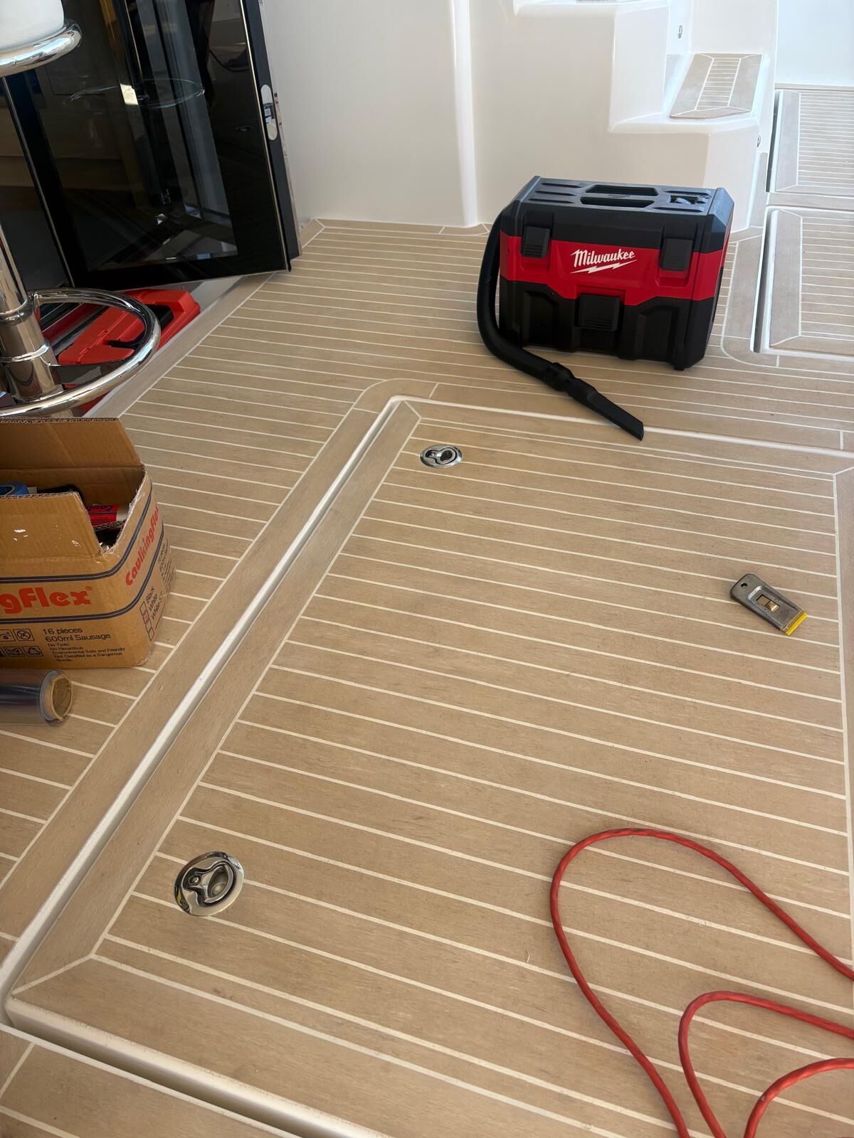 Deck hatch and lifting rings cut into new synthetic teak with caulk cartridges and a vacuum still on deck