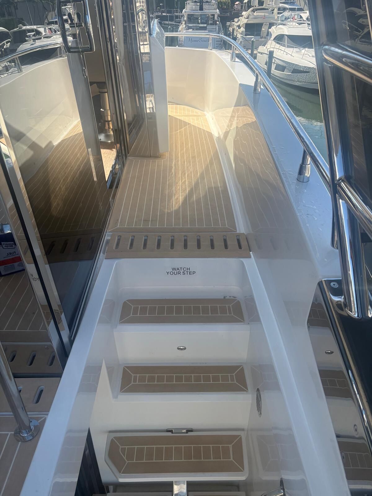 Narrow yacht side deck in synthetic teak leading to moulded steps with teak treads, marina beyond