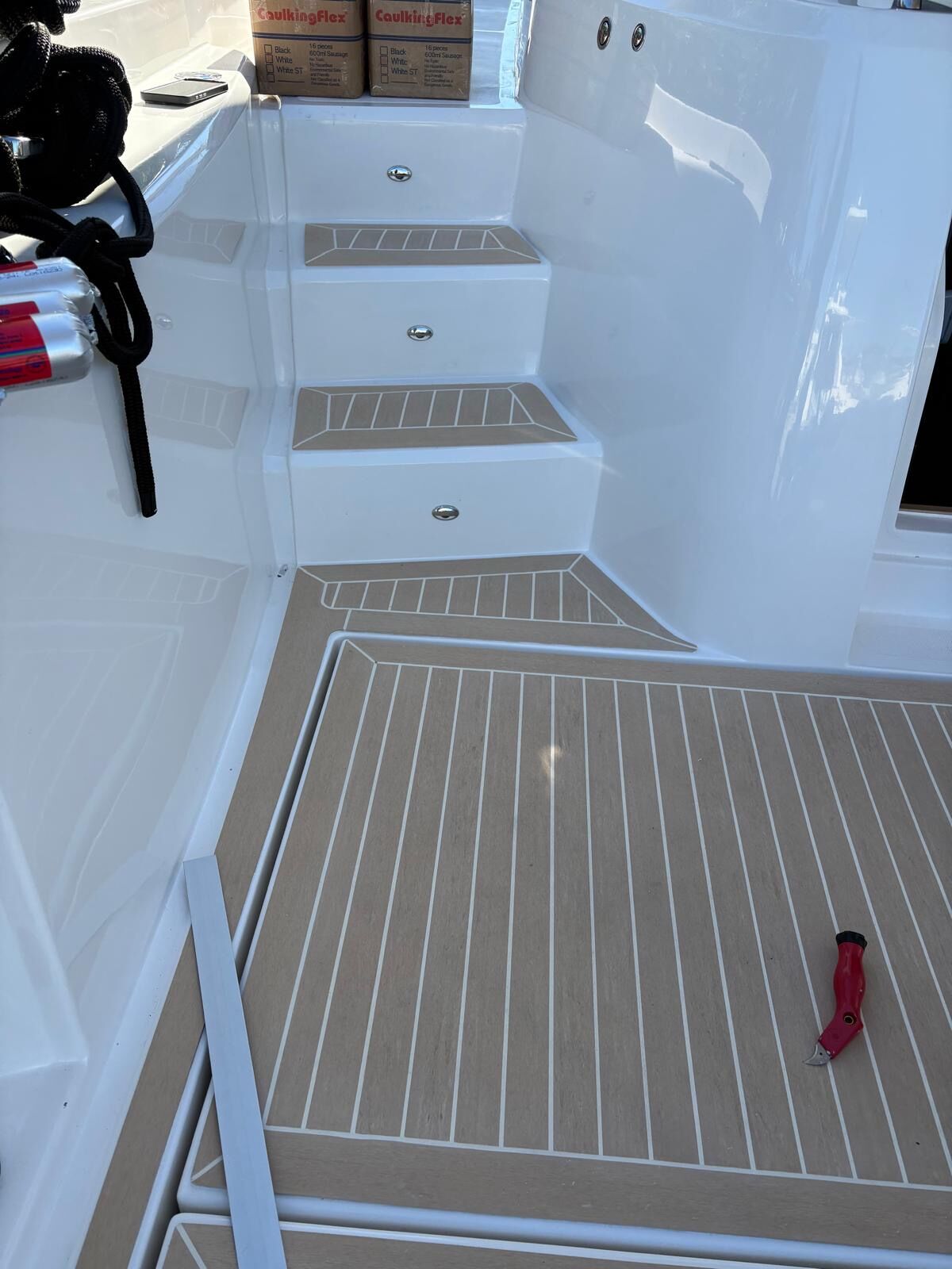 Sand-toned synthetic teak treads bonded to moulded transom steps with caulk cartridges stacked alongside