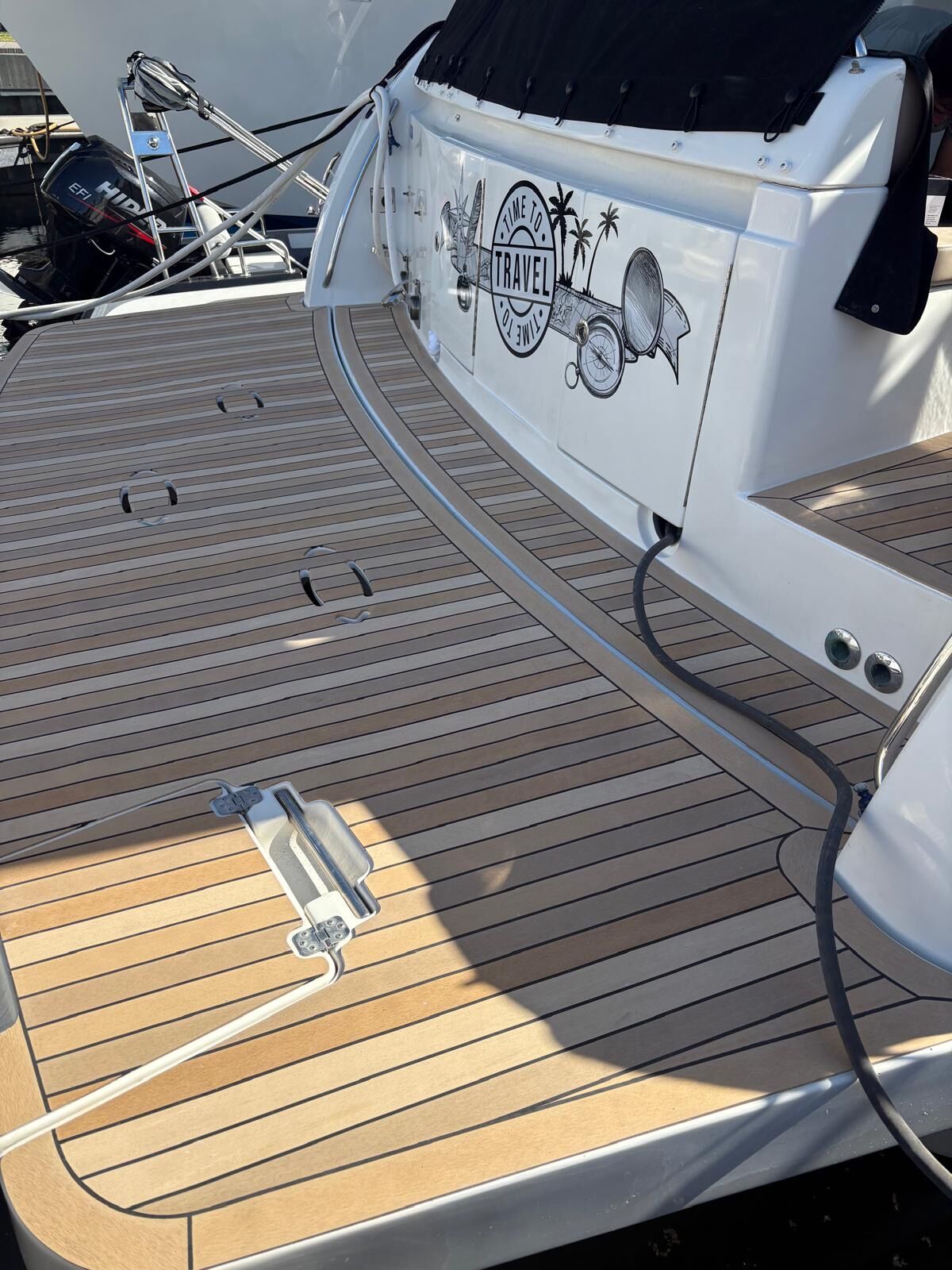 Aft deck of an express cruiser laid in synthetic teak with flush cleats and a hinged boarding gate