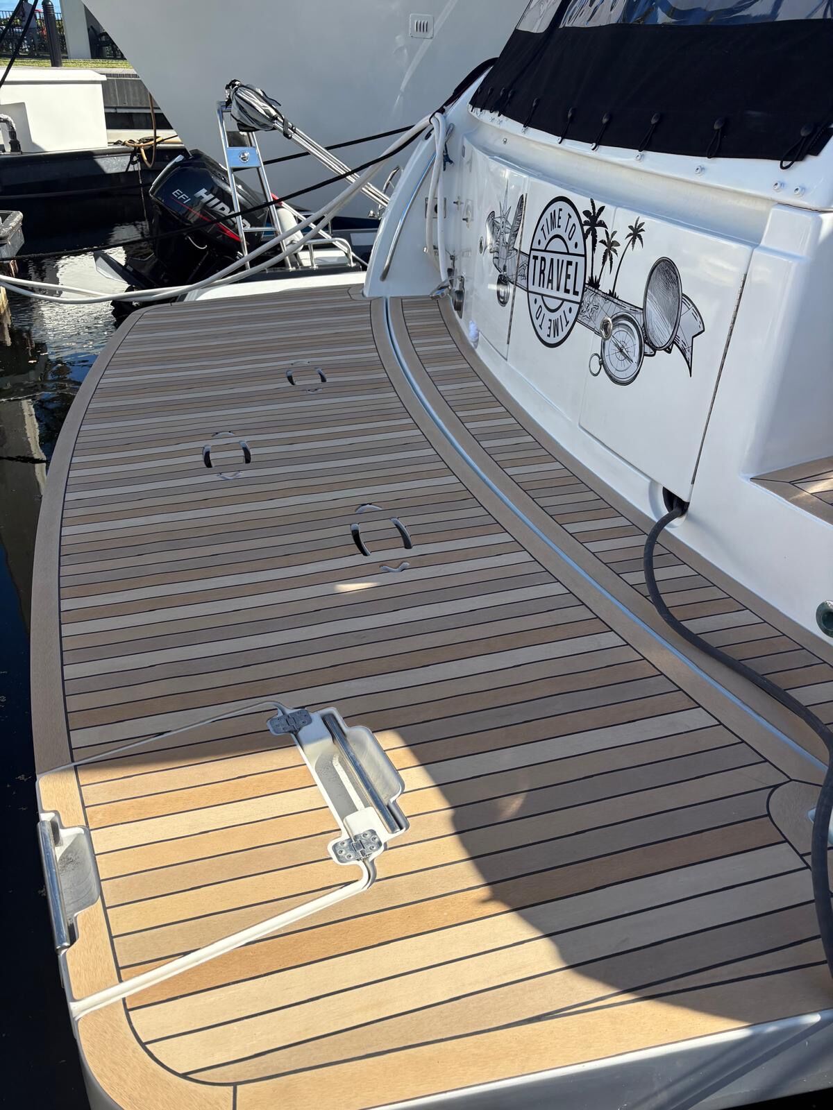 Curved side deck in synthetic teak with black caulk lines sweeping past the boarding gate of an express cruiser