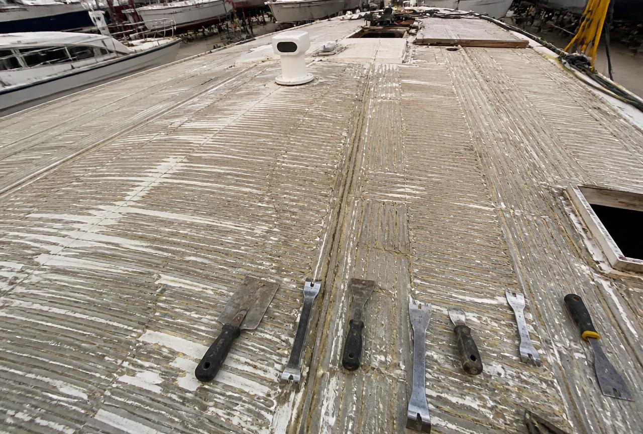 Yacht deck stripped of old teak showing adhesive residue and scrapers laid out